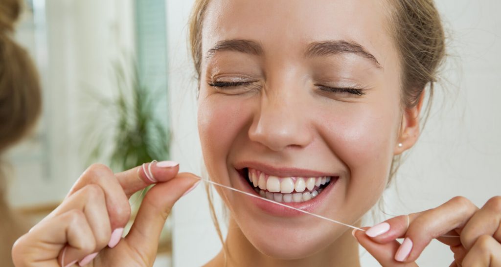 A young woman showing off her smile while holding dental floss.